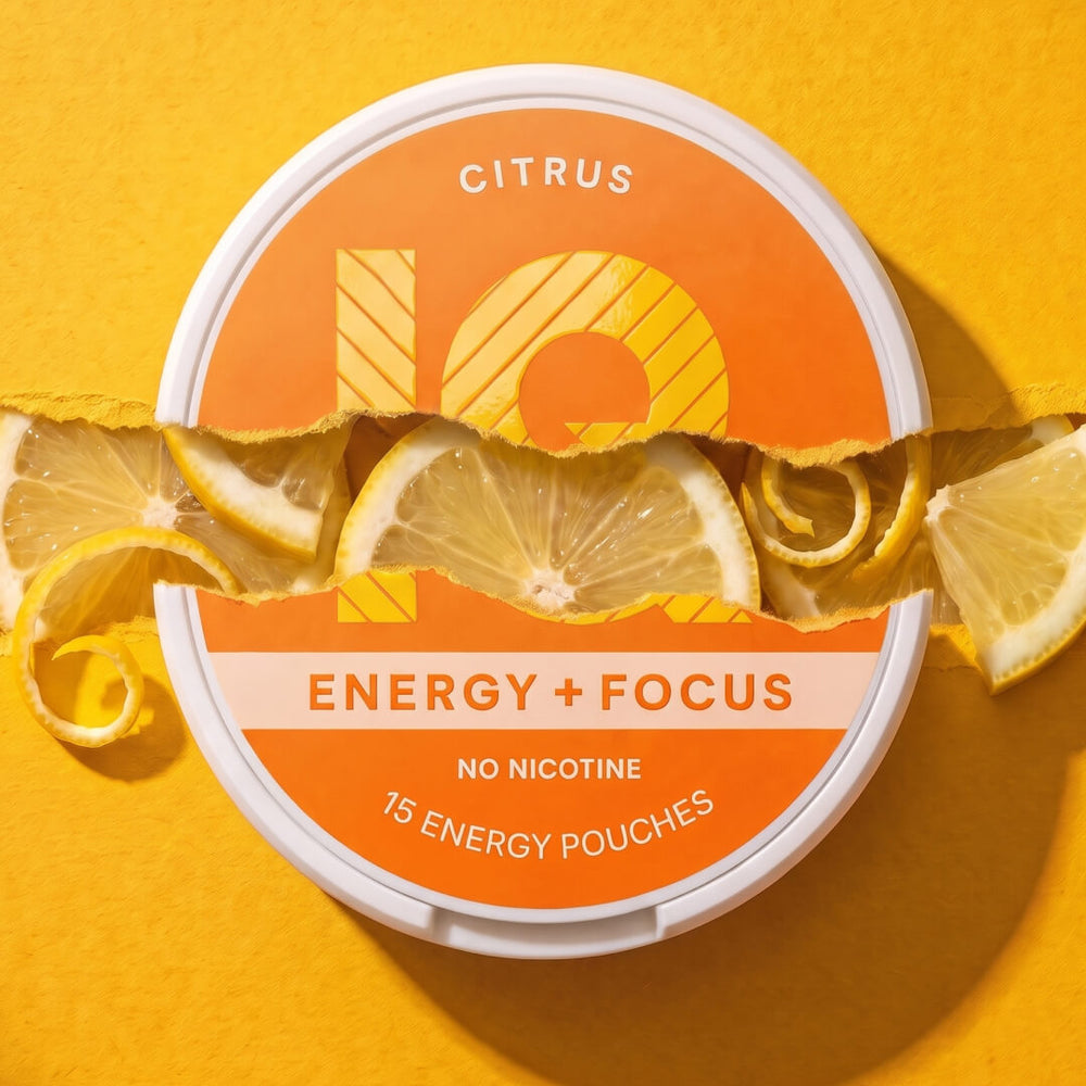 A round tin of IQ Citrus Energy + Focus pouches, shown on a bright yellow background with torn lemon slices and citrus curls layered across the front. The label is orange and white with the 10Q logo and text reading 'CITRUS', 'ENERGY + FOCUS', 'NO NICOTINE', and '15 ENERGY POUCHES'.